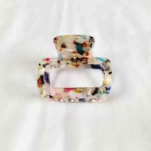 Detail of a rectangular acetate hair claw with colorful marble textures on white fabric