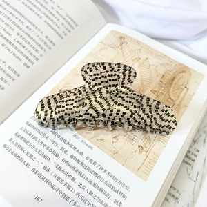 Detail of a large checkerboard hair claw clip placed on a book page for French styling