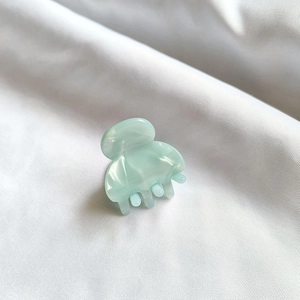 Mini mint green acetate hair claw clip with marble texture on white fabric