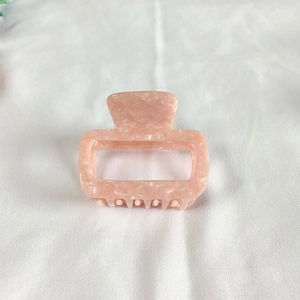 Detailed macro view of small pink marble acetate hair claw clip on white fabric
