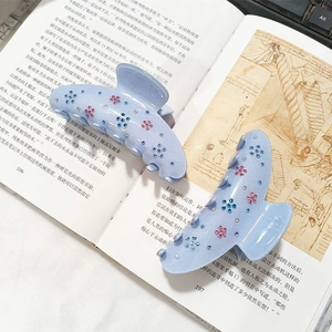 Pince à cheveux mate bleu clair avec strass floraux posée sur des pages de livre vintage