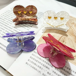 Set of four colorful heart acetate hair claws with gold accents on an open book