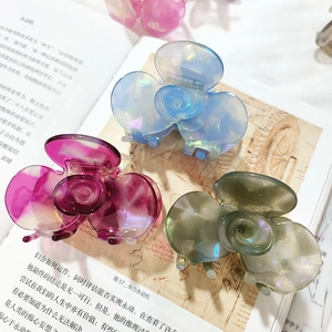 Three elegant French floral hair claws in iridescent blue, purple and green on a book