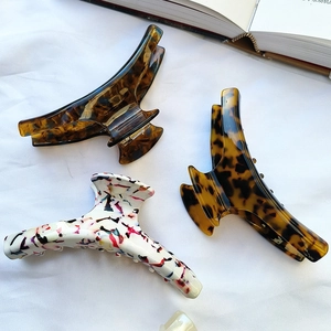 Three large acetate hair claws in amber, leopard, and floral patterns on white fabric