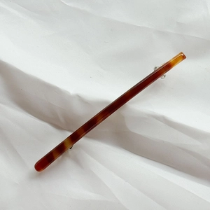 Close-up of a large amber acetate hair clip with a silver metal spring fastener on white fabric
