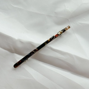 Macro shot of a long tortoiseshell acetate hair clip with metal spring on white fabric
