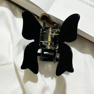 Detail showing high-gloss black butterfly acetate hair claw clip on soft white fabric