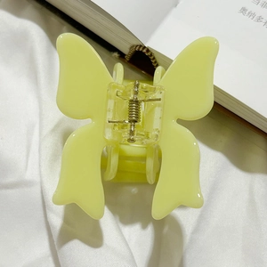 Close-up of a light yellow butterfly-shaped acetate hair claw clip on a white fabric background