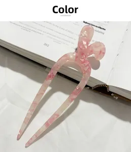 Forcina a U in acetato marmorizzato rosa e crema appoggiata su un libro aperto