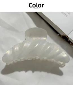 Detail of a large shell-shaped hair claw with pearlescent finish on white fabric
