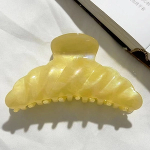 Detail view of large yellow hair claw with pearlescent shell texture on white fabric