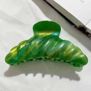 Detailed close-up of large emerald green marble shark hair claw with gold shimmer finish