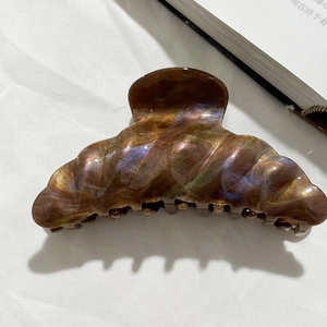 Detail of a large iridescent purple and gold hair claw clip on a clean white background