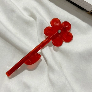 Détail d'une pince à cheveux fleur en résine rouge avec cristal sur tissu blanc