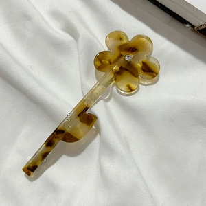 Détail de la pince à cheveux fleur en écaille ambrée avec cristal sur tissu blanc doux