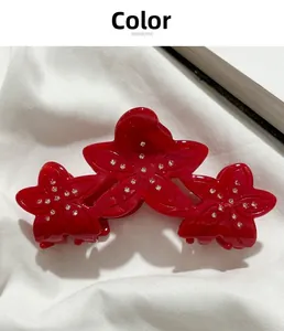 Detail of red acetate flower hair claw clip with rhinestones on white fabric