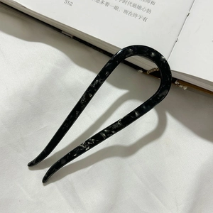 Close-up of a marble patterned acetate U-shaped hair pin on an aesthetic book background