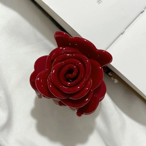 Detailansicht einer glänzenden dunkelroten Rosen-Haarklammer auf einem Buch
