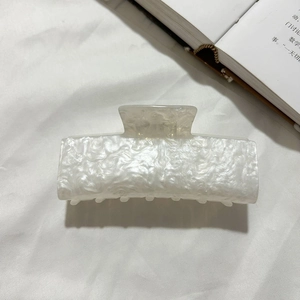 Détail d'une pince à cheveux carrée en acrylique avec texture marbrée sur tissu blanc
