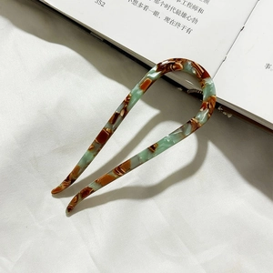 Detailed shot of acetate U-shaped hair pin with green marble texture on a book