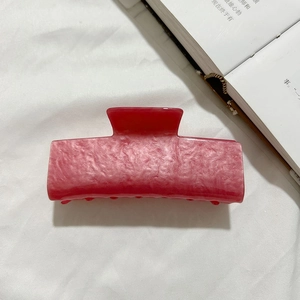Gros plan sur une pince à cheveux en acrylique rose marbré sur fond de tissu blanc doux