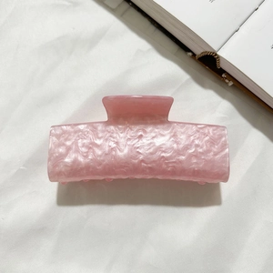 Gros plan d'une pince à cheveux en acrylique rose marbré sur un tissu blanc doux