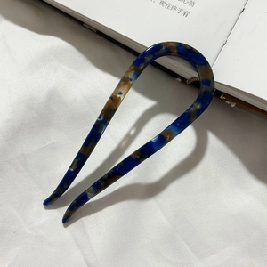 Macro detail of tortoiseshell U-shaped hair pin in deep blue acetate on white fabric