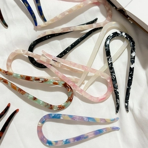 Elegant U-shaped acetate hair pins in various patterns on a minimalist white fabric background