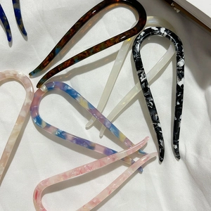 Minimalist acetate U-shaped hair pins in various marble patterns on white fabric background