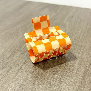 Detailed close-up of orange checkerboard hair claw clip with silver metal spring