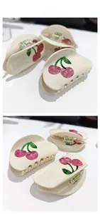 Detail view of the cherry pattern and golden metal spring on the cream hair claw clip
