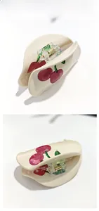 Detail view of cream hair claw clip with red cherry patterns and gold metal springs