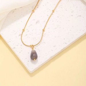 Elegant gold snake chain necklace with grey teardrop stone pendant on stone slab