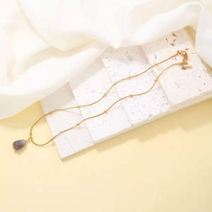 Detail view of a gold beaded chain necklace with a gray teardrop stone on white marble