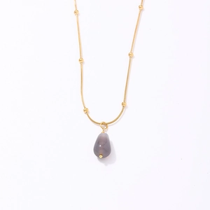 Minimalist gold necklace with a grey teardrop stone pendant and small beads on a white background