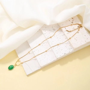 Close-up of azure teardrop necklace with golden beaded chain on elegant white fabric