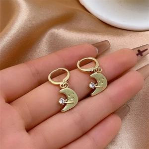 Détail de boucles d'oreilles lune souriante avec zircon sur un tissu en soie champagne