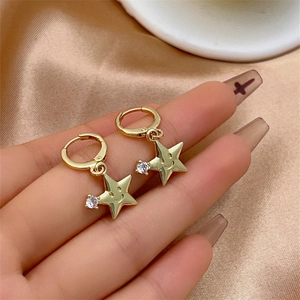 Détail de boucles d'oreilles étoile dorées avec smileys en zircon sur fond satiné