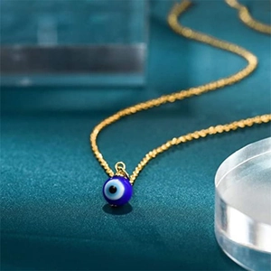 Collana dorata con ciondolo a sfera occhio turco blu su sfondo scuro testurizzato