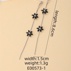 Detail view of long silver tassel earrings with black zircon flowers on yellow background