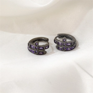 Détail de créoles en métal noir avec pierres en zircone violette sur tissu blanc