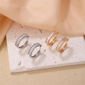 Close-up of gold and silver hoop earrings with rectangular cubic zirconia on a stone base