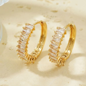 Macro shot of gold-plated hoop earrings featuring baguette-cut zircon stones on a stone base