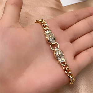 Detail of gold-plated cuban link bracelet with white zircon leopard heads on satin