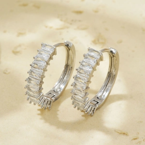 Detail of silver hoop earrings with baguette-cut zircon stones on a stone surface