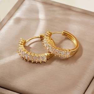 Elegant gold hoop earrings with baguette-cut zircon stones on a champagne silk background