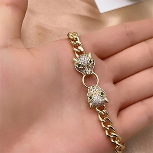 Close-up of golden leopard head Cuban chain bracelet with green gemstones and white zircons