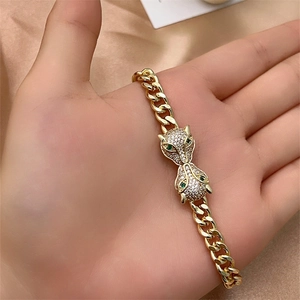 Detail of gold Cuban chain bracelet featuring double diamond leopard heads with green eyes