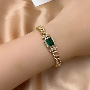 Luxury gold plated Cuban chain bracelet with emerald green stone on silk background