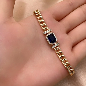 Detailed close-up of golden Cuban chain bracelet with rectangular blue gemstone and diamonds